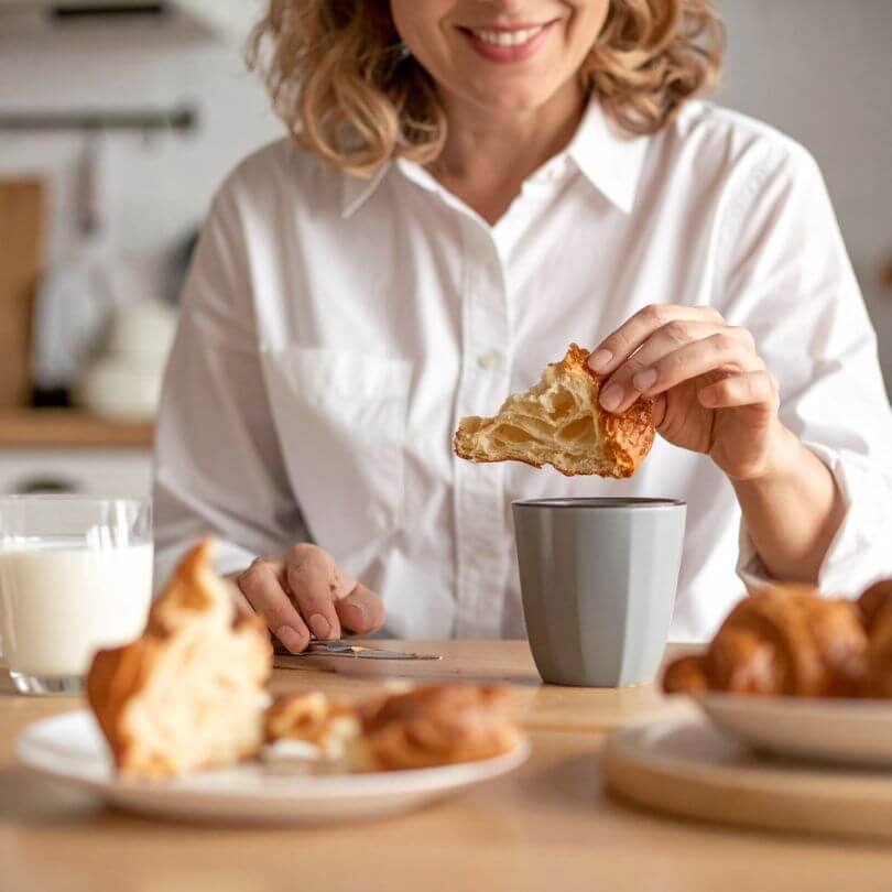 Una donna che gusta un cornetto con una tazza, mostrando l'autenticità di 15 Cornetti Zero Edizione sfoglia.