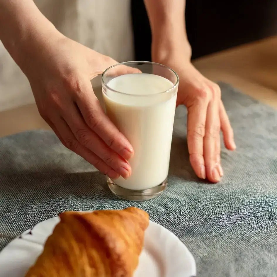 Un bicchiere di latte fresco su un tavolo accanto a un croissant, pronto per una colazione sana.
