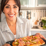 Donna sorridente che presenta una pinsa con prosciutto e jalapeños in cucina moderna.