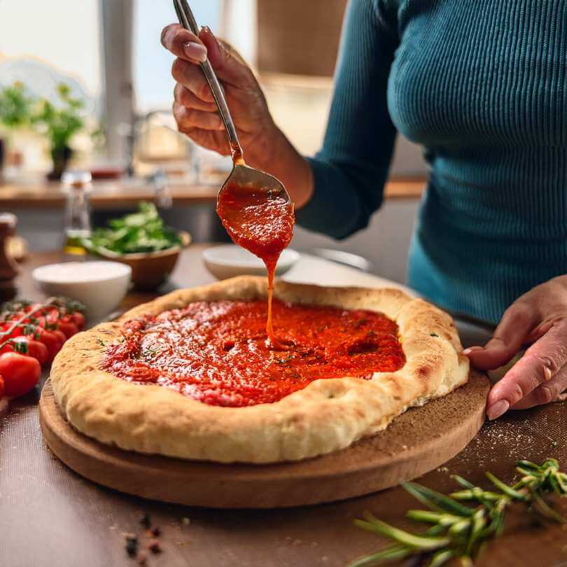 Pizza con salsa di pomodoro preparata in cucina con ingredienti freschi e aromi.