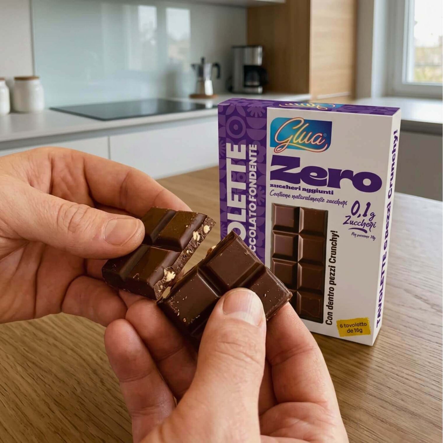 Tavolette di cioccolato fondente in una mano, confezione Glua Zero sul tavolo, ideale per dieta chetogenica.