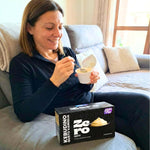 Donna che gusta Kebudino proteico alla Vaniglia su divano, con budino e confezione in vista.