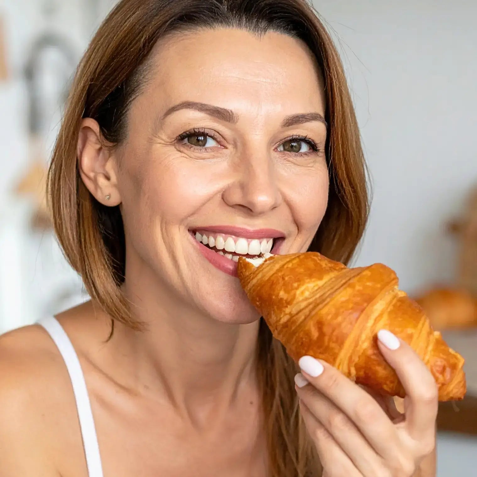 Donna sorridente che mangia un cornetto, perfetto per la dieta chetogenica, gustando 15 Cornetti Proteici Ripieni all'albicocca.